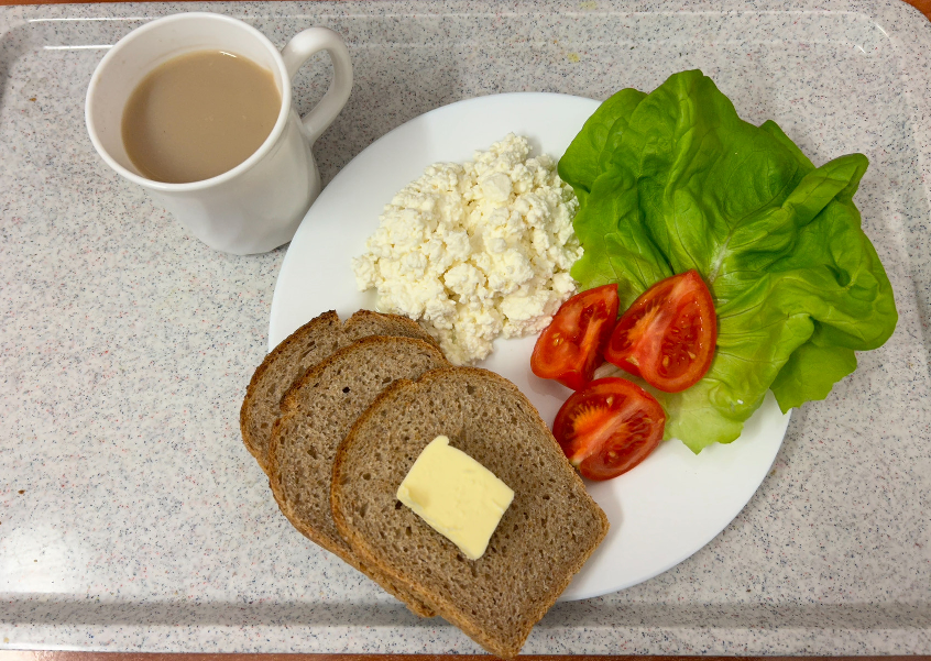 Na zdjęciu znajduje się: Kawa z mlekiem, Chleb Graham, Masło extra 82%, Twarożek, Pomidor, Sałata zielona